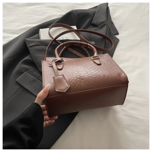 Detail of brown crocodile embossed leather handbag with twin handles and gold branding