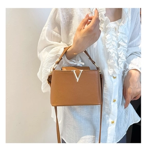 Close-up of brown leather bucket bag with silver V-shaped metal logo and textured finish