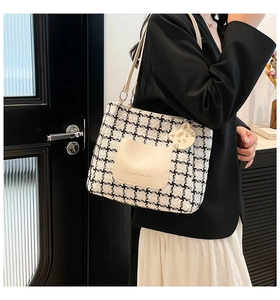 Close-up of houndstooth tote bag featuring a beige leather pocket and cat charm