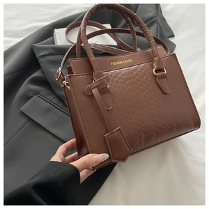 Detailed view of brown crocodile-embossed leather handbag with gold buckle and logo