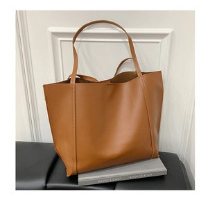 Dettaglio della borsa tote in pelle marrone con spalline sottili su base di libro grigio