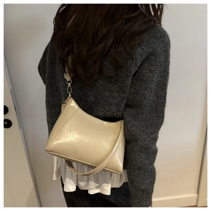 Detail of beige glossy shoulder bag with triangular stitching and gold metal buckles