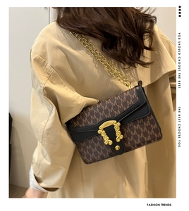 Detail of vintage crossbody bag with gold chain strap and textured flap closure on model