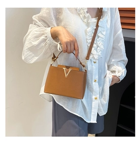 Caramel leather bucket bag with V-shaped gold metal decor shown as a crossbody