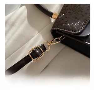 Close-up of golden metal hooks and adjustable strap buckle on embossed leather bag