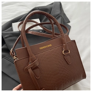 Close-up of brown crocodile texture handbag with gold hardware and top handle detail