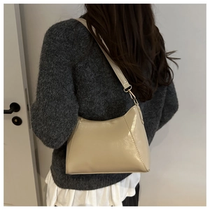Cream patent leather shoulder bag with glossy finish and gold buckle on a knitted sweater
