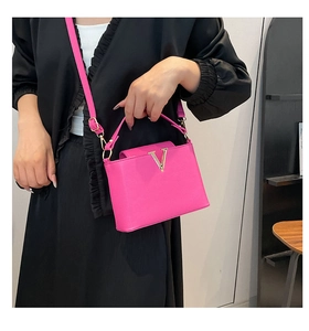 Detailed close-up of hot pink bucket bag with golden V-buckle and textured finish