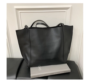 Detail of minimalist black leather tote bag with sturdy dual shoulder straps on a seat