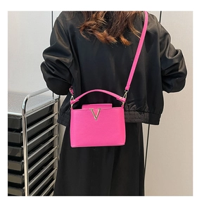 Detail of fuchsia leather bucket bag featuring a gold V-shaped buckle and crossbody strap