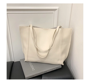 Detailed view of cream leather tote bag stitching on dark cushion with minimalist books