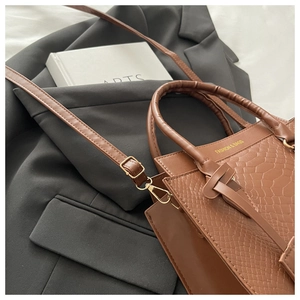 Detail of caramel brown crocodile textured handbag with sleek handle and metal strap buckle
