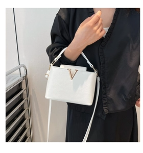 Detail of white leather bucket bag with gold V-decoration and adjustable shoulder strap