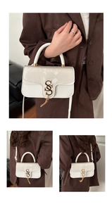 Detail of cream crossbody bag with snakeskin flap, gold S-lock and tassel charm detail