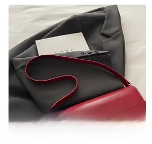 Detail of red leather handbag with gold horsebit buckle on a grey blazer backdrop
