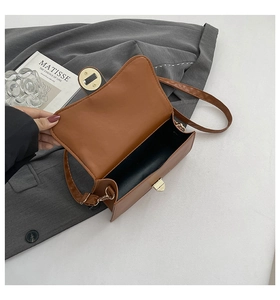 Detail view of brown faux leather crossbody bag with golden turn-lock closure on grey suit