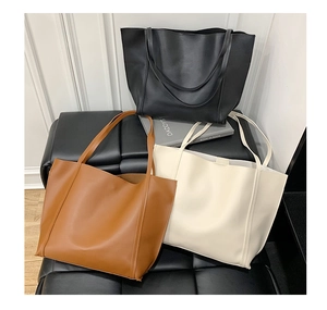 Three classic minimalist tote bags in black, brown, and off-white on a sleek black sofa