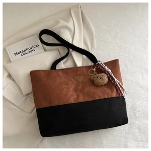 Detalle de bolso tote de ante con logo metálico, colgante de oso y diseño bicolor de otoño