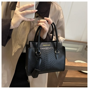 Detail of black faux crocodile leather handbag featuring elegant gold lettering on a trench coat