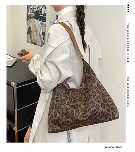 Chic leopard print suede hobo bag with brown leather strap worn by a model