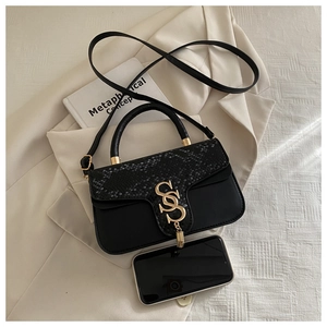 Detail of black snake-pattern leather bag with gold metal clasp and tassel on white jacket