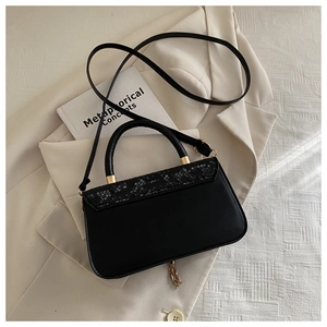 Close-up of black handbag with snakeskin pattern flap and gold tassel detail