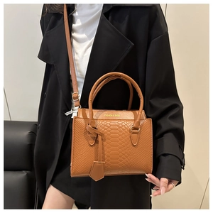 Braune Handtasche mit Schlangenprägung und Schultergurt auf schwarzem Mantel