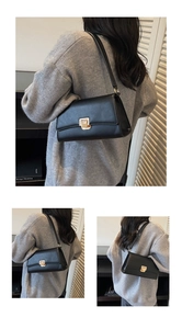 Detail of minimalist black leather baguette bag featuring a gold square metallic lock
