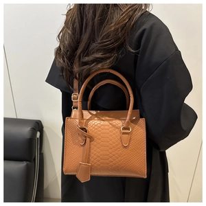 Detail of brown crocodile embossed leather handbag with adjustable strap and gold hardware