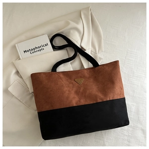 Detalle de un bolso tote en contraste marrón y negro con logo triangular dorado en ante