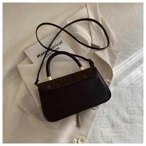 Detail of dark brown handbag with snake pattern flap and gold tassel on office attire