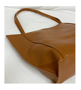 Close-up of caramel brown tote bag showing matte leather texture and precise stitching