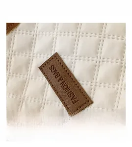 Close-up of quilted pattern and brown leather brand patch on warm white tote bag