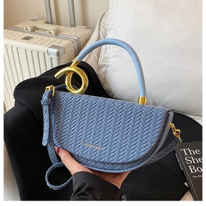 Close-up of sky blue woven saddle bag featuring a modern gold metal ring handle
