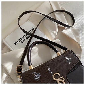 Detail of snake embossed leather handbag with gold CS logo on a beige blazer