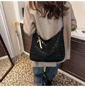 Detail of a black leopard print hobo bag with a beaded tassel charm on a shoulder strap