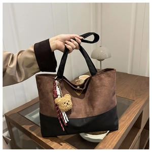 Brown suede tote bag with black strap and cute teddy bear pendant in home setting
