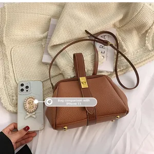 Close-up of brown litchi grain leather bag with gold twist lock next to an iPhone