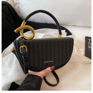 Detail of black woven leather saddle bag featuring a gold metal ring handle and strap