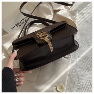 Detail of dark brown leather handbag with snake pattern texture and gold tassel charm