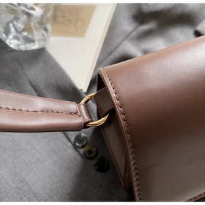 Detailed close-up of brown leather bag strap with golden metal ring and precise stitching