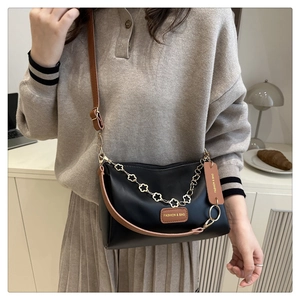 Detail of elegant black and brown crossbody bag with gold floral chain and embossed logo
