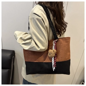 Detail of a large brown and black tote bag featuring a teddy bear charm and webbed handles