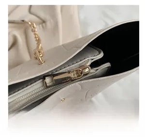 Detail shot of golden metal zipper and chain hook on beige crocodile embossed tote bag