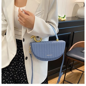 Close-up of blue woven saddle bag with gold metal ring handle and fashion logo