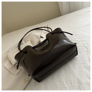Detail of high-gloss dark coffee tote bag featuring a knotted strap on white fabric