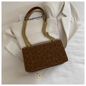 Detail of leopard print suede shoulder bag with gold chain strap on beige blazer