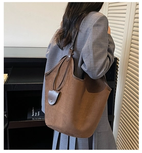 Detail of a large brown suede tote bag with leather trim worn on the shoulder by a model