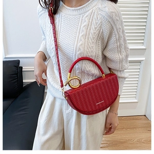 Close-up of red woven saddle bag with gold metal handle and embossed fashion logo