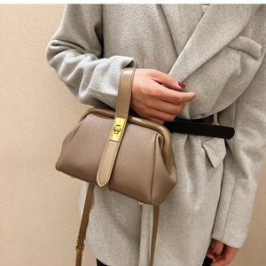 Detail of camel lychee leather doctor bag with gold metal clasp on a grey coat